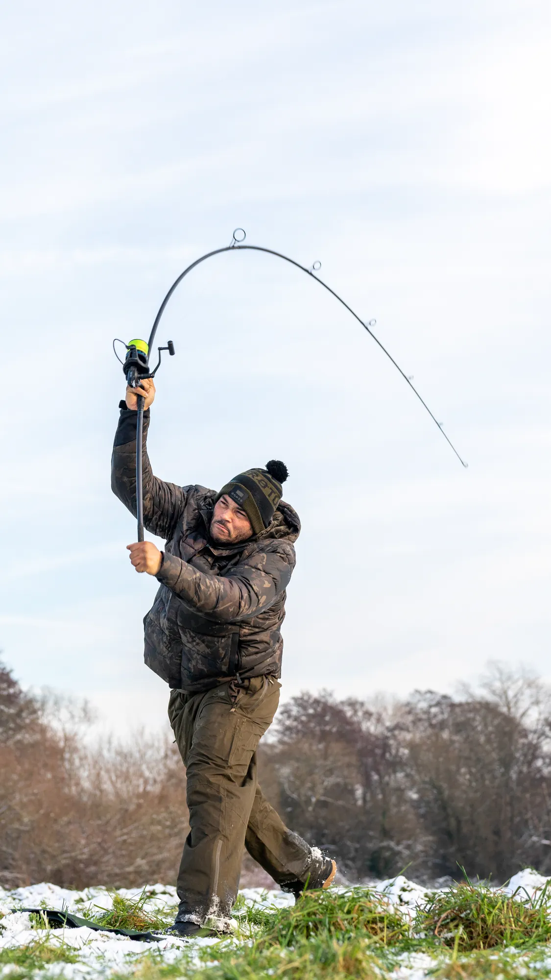 Jermaine Hull in full casting follow-through in a snowy field, rod bent hard