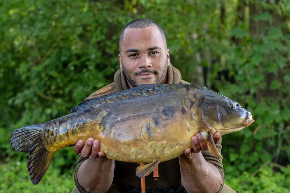 Jermaine holding a mirror carp against green foliage